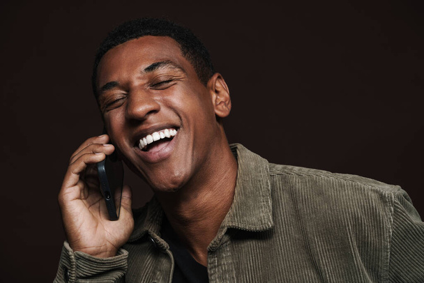 Young black man laughing while talking on mobile phone isolated over brown wall - Foto, Bild