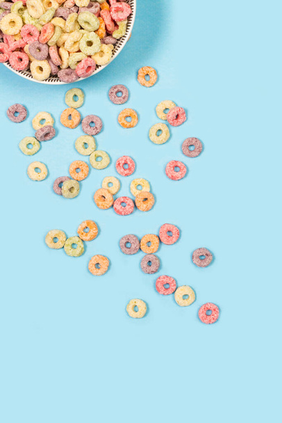 Cereales con sabor a fruta en un tazón y sobre un fondo azul claro con espacio para copiar - Foto, imagen