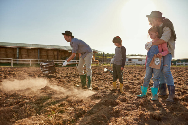 Mother, daughter and son looking at father digging ground with shovel on plow field for planting seeds on ranch or farm. Eco harvest. Environment sustainability. Modern village lifestyle. Agriculture - Fotografie, Obrázek