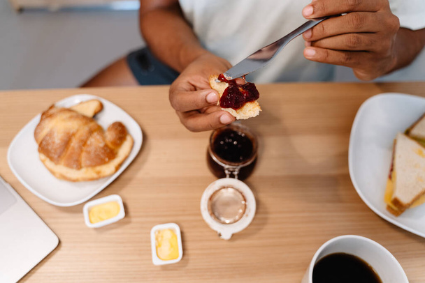 Black man eating croissant with jam while having breakfast in hotel - Photo, Image