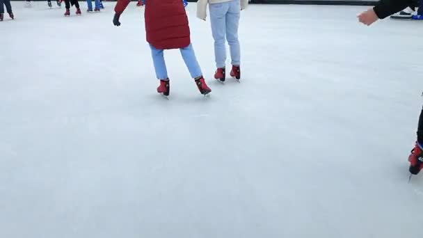 Menschen, die an einem Wintertag in der Stadt auf der öffentlichen Eisbahn unter freiem Himmel Schlittschuh laufen. Menschen beim Schlittschuhlaufen auf der Eisbahn. Beine, Rücken, Eisbahn. Winterurlaub, Aktivitäten, Erholung, Erholung, Sport - Filmmaterial, Video