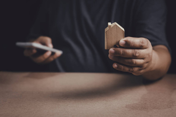 Man hand holding wood house model with using smartphone to Planning buy Real Estate, Planning to buy property investment and house mortgage financial concept. - Fotoğraf, Görsel