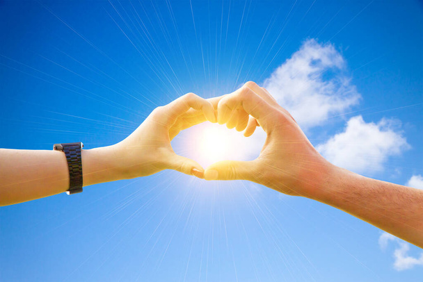 Το ζευγάρι της αγάπης κρατά τα χέρια ψηλά στον ουρανό σε σχήμα καρδιάς γύρω από τον ήλιο. - Φωτογραφία, εικόνα
