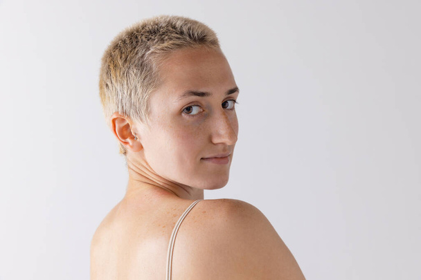 Close-up portrait of young short-haired blonde girl posing, looking at camera isolated over grey studio background. Concept of beauty, body and skin care, health, plastic surgery, cosmetics, ad - Φωτογραφία, εικόνα