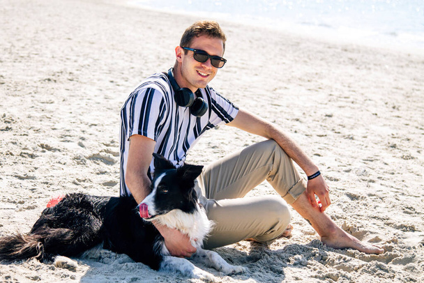 relaxed man on the beach enjoying with his dog and listening to music with headphones - 写真・画像