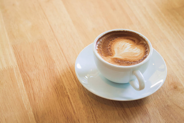 Café con leche caliente en forma de corazón en una taza blanca colocada en un piso de madera. Copiar espacio - Foto, Imagen