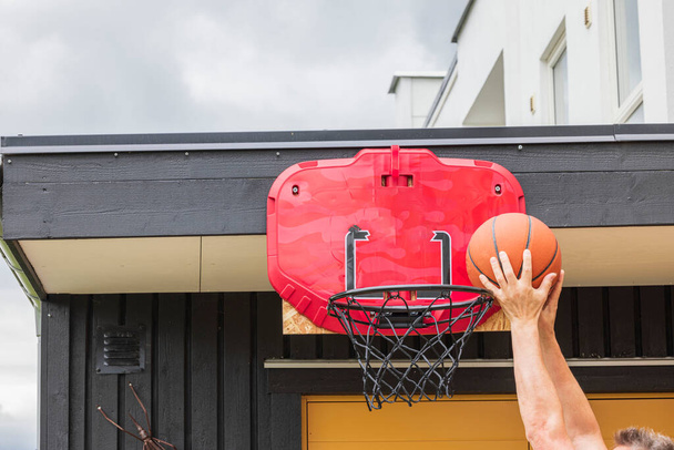 Вид людини, яка забиває м'яч в баскетбольний обруч з сіткою під час гри в баскетбол. Швеція. - Фото, зображення
