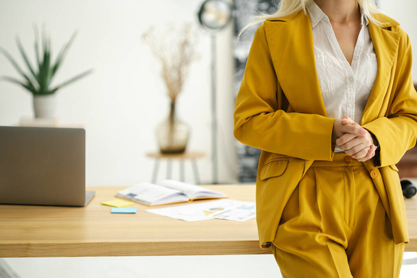 Fondo de oficina de mujer de negocios, lugar de trabajo, mujer en traje amarillo brillante de pie cerca de la mesa de oficina, espacio de copia - Foto, imagen
