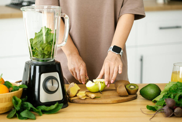 Nainen laittaa aamiaista vihreästä tuoreesta smoothie keittiössä, lähikuva. Valmistelu luonnollinen detox limonadi pöydässä keittiössä - Valokuva, kuva