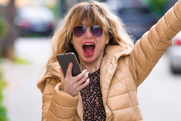 jubilant and euphoric woman on the street looking at the mobile phone - Foto, Imagen