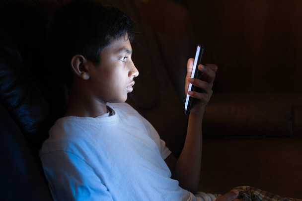  teenage boy sitting on sofa using smart phone at night . - Photo, image