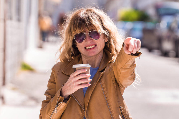 adult woman with coffee on the street and pointing a direction - Foto, Imagem
