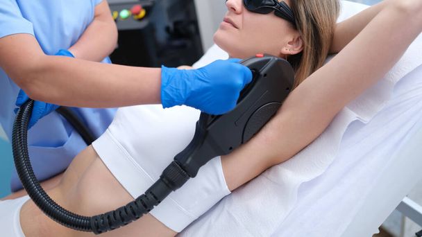 Young woman undergoes laser hair removal procedure in beauty salon. Armpit hair removal concept - Φωτογραφία, εικόνα