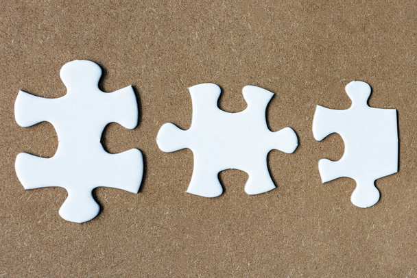 Three pieces of white jigsaw puzzle on wooden background. Directly above. Flat lay. Copy space. - Foto, imagen