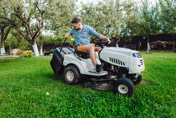 Gardener worker using lawn tractor and cutting grass through garden - Foto, afbeelding