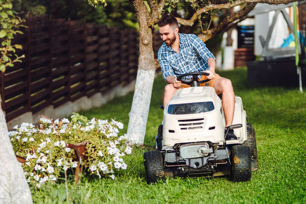 Man using lawn tractor for mowing grass in household garden. Landscaping works with professional tools - Foto, imagen