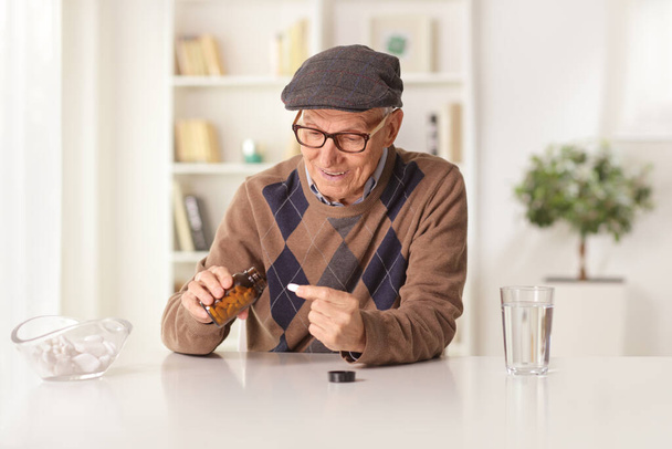 Pensioner sitting at home and taking a pill out of a bottle - Foto, afbeelding