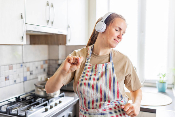 Smiling beautiful woman dancing in kitchen listening music with headphones. - Photo, image