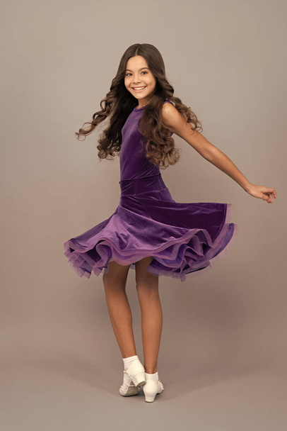 веселый ребенок с длинными вьющимися волосами танцует в бальном платье на всю длину, quickstep. - Фото, изображение