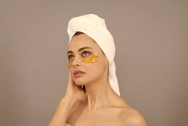 Skin with the shine. girl reduce eye bags. skincare. facial collagen cosmetic. moisturizing skin. cosmetology. young woman in towel use patch. beauty day in spa. applying golden anti-fatigue mask. - Photo, Image