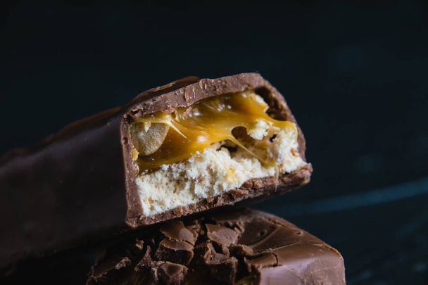 Delicious chocolate bar with caramel and peanuts close up on dark concrete background with copy space. - Φωτογραφία, εικόνα