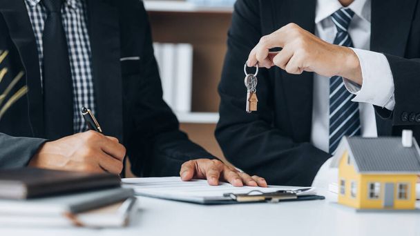 A home rental company employee is handing the house keys to a customer who has agreed to sign a rental contract, explaining the details and terms of the rental. Home and real estate rental ideas. - Foto, Bild