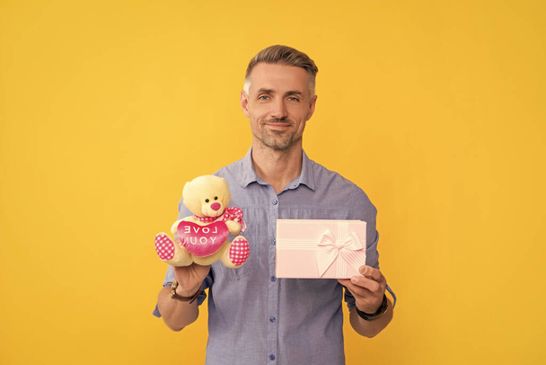 счастливый горький парень, держащий коробку и игрушку на желтом фоне, любовь. - Фото, изображение