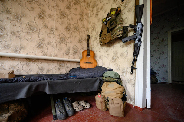 ギターの横にある兵士の戦闘軍事攻撃ライフルAK 74と軍事弾薬、ウクライナの戦争、折り畳まれた軍事靴. - 写真・画像