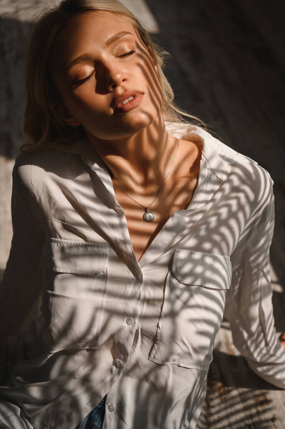 Delicate and sensual blonde in a white silk blouse and with a decoration around her neck - Foto, imagen