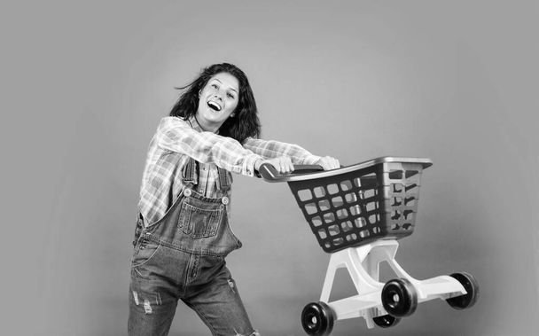 smiling female hipster with trendy clothes carry shopping cart, cyber monday. - Photo, image