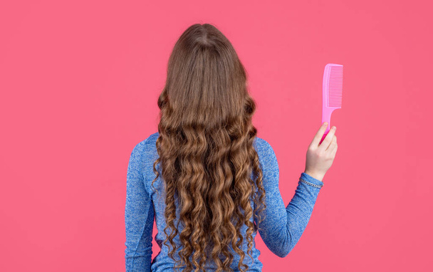 back view of teen girl with curly hair hold comb on pink background. - Foto, Imagen