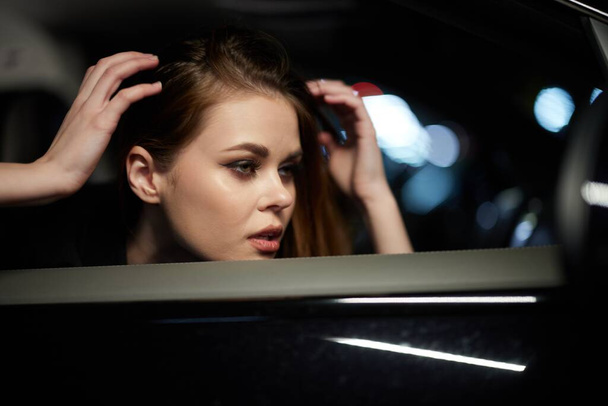 photo horizontale du côté, la nuit, d'une femme assise dans une voiture et regardant par la fenêtre, redressant ses cheveux avec ses mains. Photo de haute qualité - Photo, image