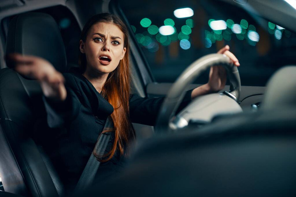 een horizontale foto van een vrouw achter het stuur van een auto met een gespannen uitdrukking steekt haar hand in de camera. Fotografie 's nachts. Hoge kwaliteit foto - Foto, afbeelding