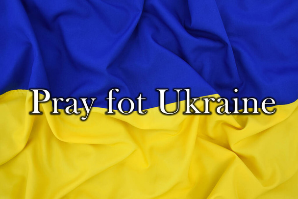 Nápis PRAY PRO UKRAJINU na pozadí státní vlajky Ukrajiny, UA. Modrá a žlutá barva. Wat na Ukrajině. - Fotografie, Obrázek
