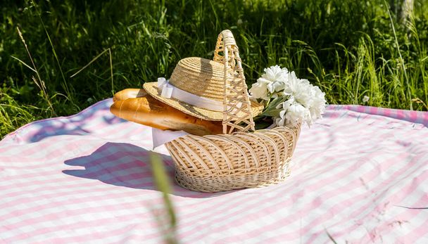 Picknickmand met stokbrood, bloemen en een strohoed in de tuin - Foto, afbeelding