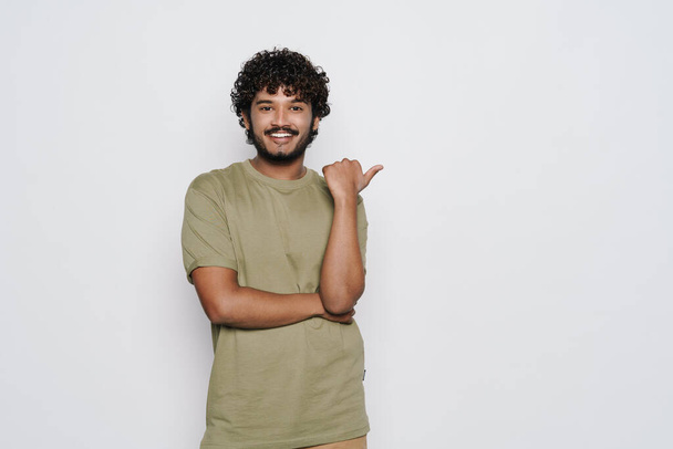 Young bearded man dressed in t-shirt smiling and pointing finger aside isolated over white background - Φωτογραφία, εικόνα