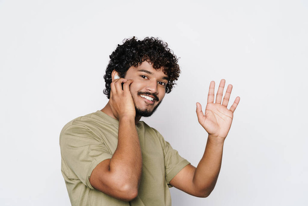 Mladý muž ze Středního východu gestikuluje při poslechu hudby se sluchátky oddělenými přes bílou zeď - Fotografie, Obrázek