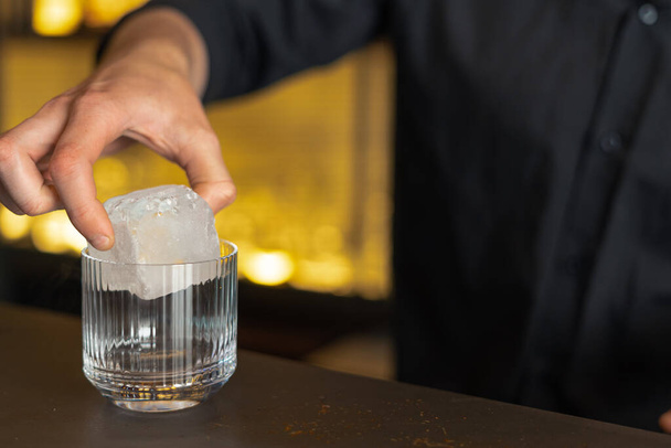 Ο μπάρμαν ετοιμάζει ένα κοκτέιλ σε ένα μπαρ, κλαμπ. Ρίχνει αλκοόλ και σιρόπια. χρησιμοποιεί πάγο και σπάει πάγο - Φωτογραφία, εικόνα