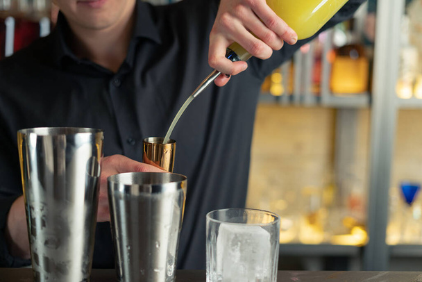 A csapos koktélt készít egy bárban, klubban. Alkoholt és szirupot önt. jeget és jeget használ - Fotó, kép
