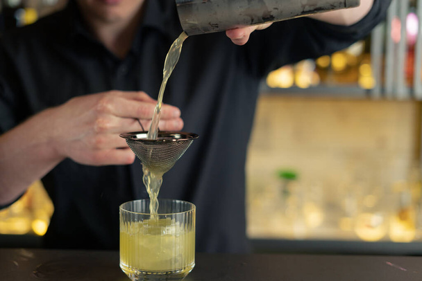 Ο μπάρμαν ετοιμάζει ένα κοκτέιλ σε ένα μπαρ, κλαμπ. Ρίχνει αλκοόλ και σιρόπια. χρησιμοποιεί πάγο και σπάει πάγο - Φωτογραφία, εικόνα