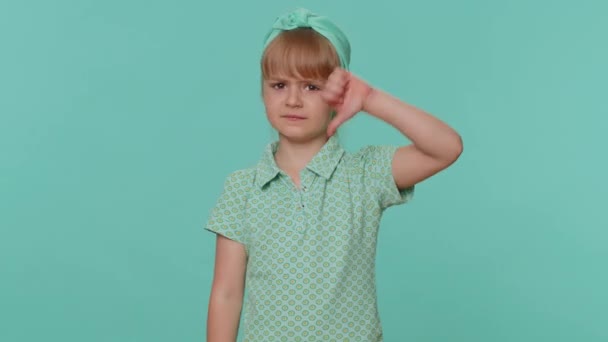 Niechęć. Zdenerwowany mały maluch dziewczynka pokazuje kciuki w dół gest znak, wyrażając niezadowolenie, dezaprobatę, niezadowolenie. Młody przedszkolak w okularach odizolowany sam na tle niebieskiego studia - Materiał filmowy, wideo