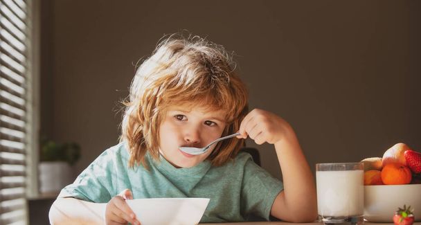Portret van een schattig kind dat soep eet of ontbijt bij de tafel thuis met lepel. Kinderen gezond voedsel - Foto, afbeelding