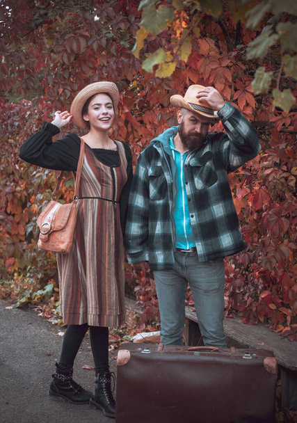 Smiling happy girl and bearded man in hat with large vintage looking bag. Guy wearing plaid shirt and femme in hipster autumnal dress. Stylish lovers. Fall hipster outfit concept - Photo, image