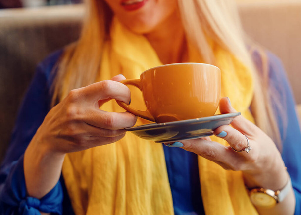 жінка в блакитній блузці і жовтому шарфі п'є каву в кафе. Думки про Україну - Фото, зображення