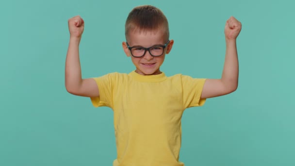 Erős és független vagyok. A kisgyerek fiú bicepszeket mutat és magabiztosnak tűnik, erőt érez, hogy harcoljon a jogokért, energiát, hogy sikert érjen el. Óvodás srác kék háttér - Felvétel, videó
