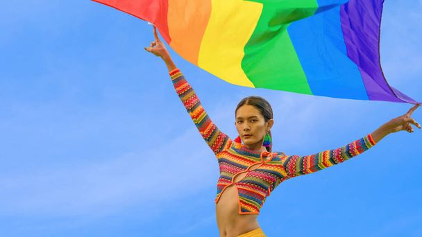 Portrait of transgender person posing with pride flag with blue sky background in celebration of pride month for human equality and diversity for lgbtq people - Foto, afbeelding
