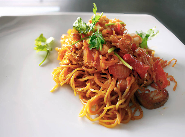 close-up roerbak noodle Thaise stijl met rode saus, tomaat, ui, paddestoel en zeevruchten op wit bord - Foto, afbeelding