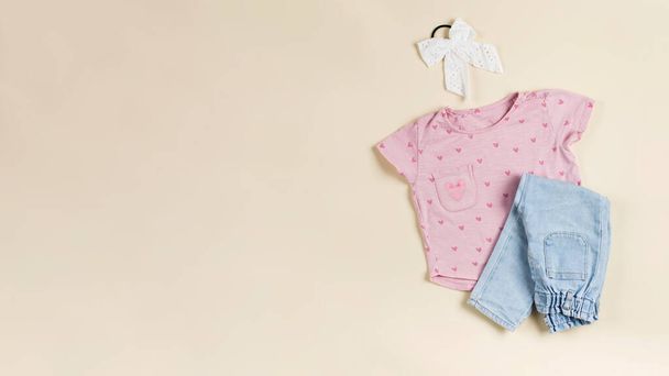 Childrens pink T-shirt and folded jeans on a beige background. Fashionable casual look for a girl. Flat lay. Banner - Foto, Bild
