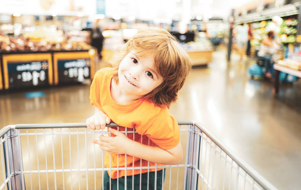 Funny customer boy child holdind trolley, shopping at supermarket, grocery store - Фото, изображение