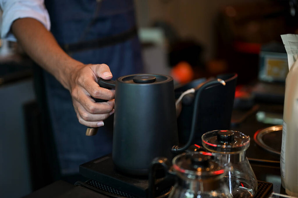 Close-up and cropped shot, Male barista holding a kettle, pouring hot water into a coffee cup with ground coffee, making a hot latte. - Photo, Image
